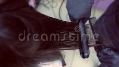 美容师在美容院用发钳给美女扎黑棕色头发。 头发特写。